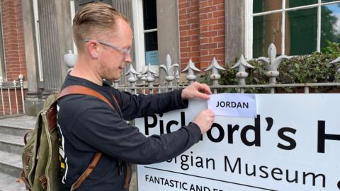 Doctor removing the name Jordan from a sign it has been crudely blutacked to