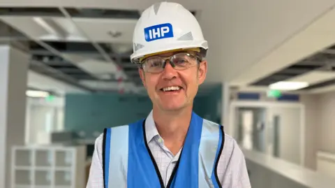 BBC/JULIA LEWIS Dr Ed Smith wearing a hard hat and a blue high visibility jacket standing in an empty hospital ward