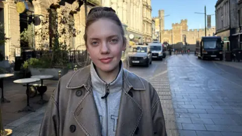 A white woman with light brown hair looking at the camera with Cardiff Castle in the background