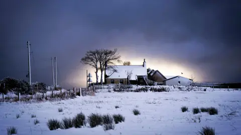 PA Media A farmhouse in a rural area with the roof and ground around it covered in snow