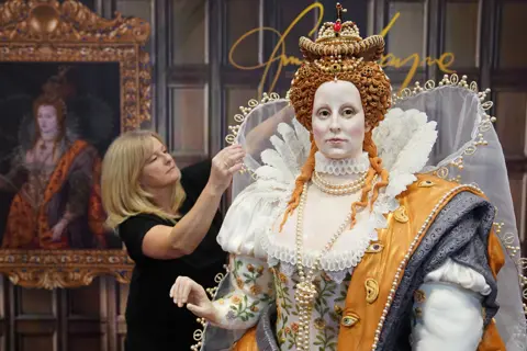 Jacob King/PA Media Cake artist Emma Jayne adjusting the outfit on her edible life-sized version of Queen Elizabeth I. The Tudor queen is wearing a crown and jewels as well as an finely embroidered dress.