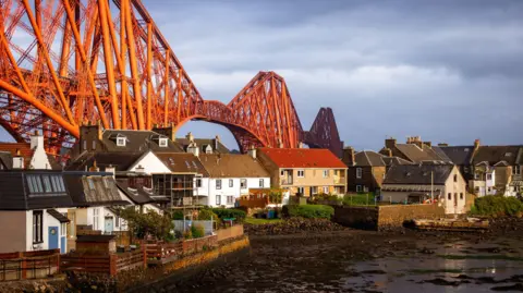 Getty Images The Forth Rail Bridge stretching behind a row of white and brown houses.