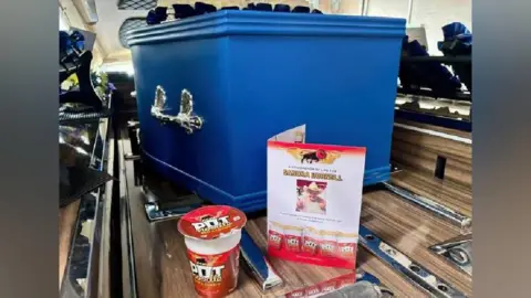 Kirsty Sailes A royal blue coloured coffin with a Pot Noodle and order of service