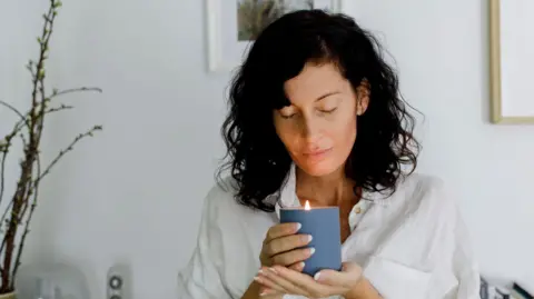 
Woman with eyes closed holding candle in living room at home