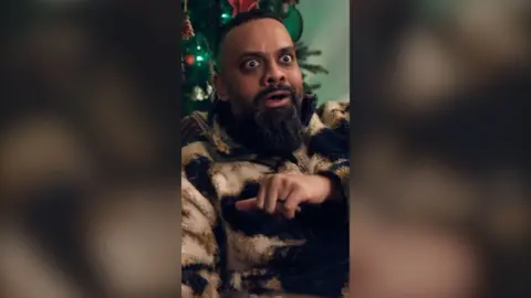 Man with beard looking excited in front of a Christmas tree