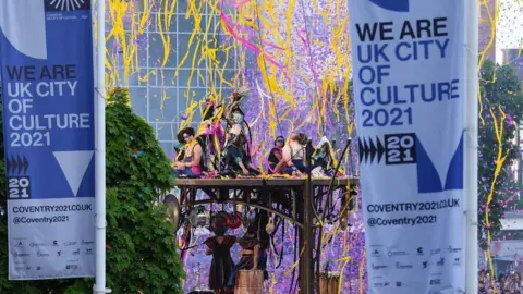 PA Media A group of dancer performing on a wooden platform in the centre of Coventry with colourful confetti and streamers in the area