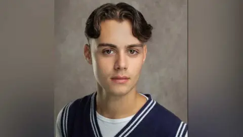 SUPPLIED Bradley Riches is looking directly at the camera. He has brown hair and brown eyes and wears a white T-shirt with a blue sleeveless tank top over the top.