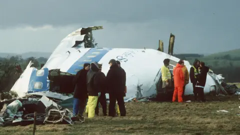 Emergency service personnel standing next to the fuselage of Pan Am flight 103 after it was downed over Lockerbie.