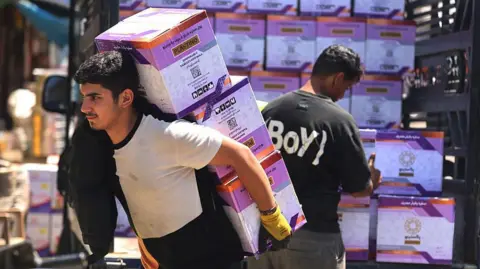 Workers unload goods from the back of a truck at the Jamila food market in Sadr City, east Baghdad on April 13, 2026. 