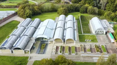 WAKEHURST An aerial image of the Millennium Seed Bank at Wakehurst made up of a number of white and grey greehouse style buildings set among lush greenery