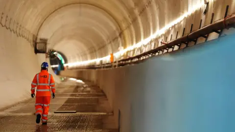A man in hi-vis clothing, branded with the logo of HS2, walks through the Chilterns tunnel