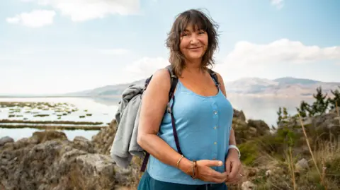 Woman in blue vest and shorts wearing a grey rucksack
