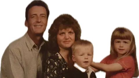 Supplied John and Wendy Little smiling at the camera with their children Callum and Kirsty. Callum has short blonde hair and is held by Wendy, who has curly brown hair with fringe and wears a top with a geometrical print. Kirsty is next to them. She wears a pink t-shirt and has long blonde hair and a fringe. John has short brown hair and wears a white shirt with small grey squares. 