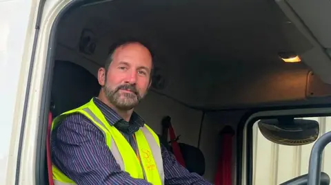A man smiles while behind the wheel of a truck