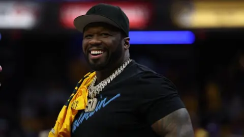 Reuters 50 Cent is pictured smiling and looking off camera. He is wearing a black baseball hat, a black T-shirt and diamond-encrusted silver chain with the numbers "50" hanging down.
