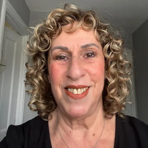 Amanda Richardson A woman with blonde curly hair and orange lipstick smiles at the camera.