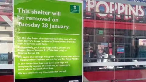 A sign on a bus shelters explains why it is being removed, whilst a bus is seen driving by.