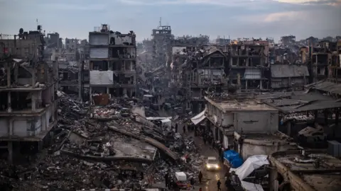 EPA Palestinians walk past destroyed buildings in the Jabalia camp, north of Gaza City.