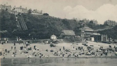 Getty Images A black and white archive image of Edwardians at the beach. In the background is a funicular. 