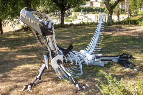 Blenheim Palace A white and black foam sculpture of Megalosaurus resting on its belly on the grass.