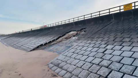 BBC Damaged sea wall defences at Aberdeen beach, much of the stonework is missing, above the sand, and the promenade is above.