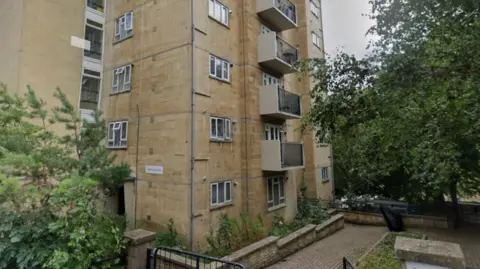 A Google Street View image shows the base of Berkeley House. Taken in summer, the tower block is surrounded by green trees. 