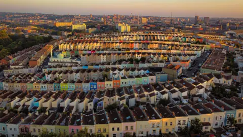The sun rises over colourful houses in Totterdown, Bristol, creating a golden glow on the rooftops. 