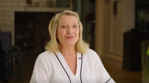 Blonde-haired Sian Astley, wearing a white top, speaks to the camera in a Reform visor