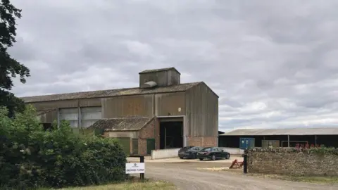 Forge Design Studio Two cars parked outside a farm building. A sign near an entrance says "George Farm"