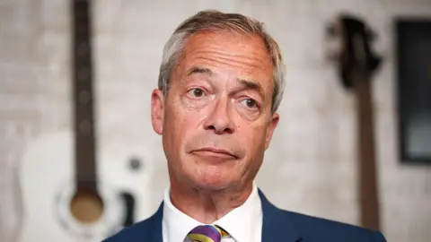 Nigel Farage in a close-up, wearing a blue suit, white shirt and stripe tie.