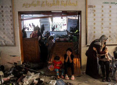Women and children sit among the damage after an Israeli strike on the school