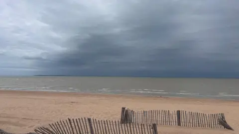 Rob Fox Smoke seen in the sky above the sea. Broken fencing can be seen on the beach.