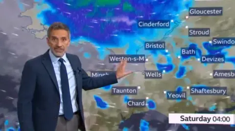 Ian Fergusson, wearing a dark blue suit, stood in front of a weather forecast map