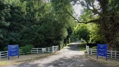 Google Entrance to school showing blue signs and driveway lined with trees