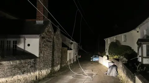 A village street in the darkness, phone lines lie across the carriageway 