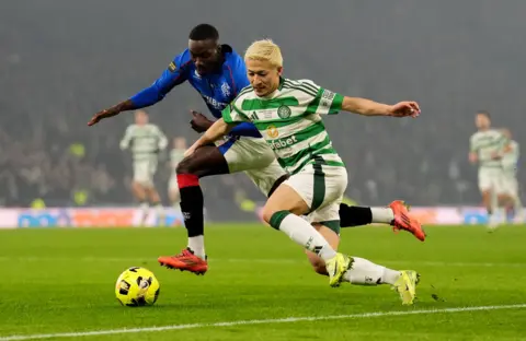 Reuters Celtic player Daizen Maeda, who is wearing a green and white hooped football tope, white an green shorts, white and green socks and yellow boots battles for the ball with Rangers midfielder Mohammed Diomande who is wearing a blue top, white and blue shorts, red, black and white socks and pink boots at Hampden Park