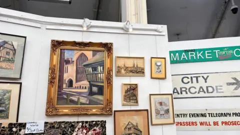 An exhibition wall showing paintings and framed prints depicting Coventry as well as antique signage.
