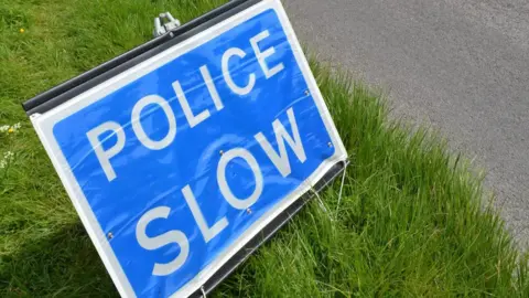 A blue sign on a patch of grass reading "police slow".