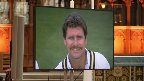 A screen in front of Winchester Cathedral's alter, with a head and shoulders picture of Robin Smith, smiling, in his cricket whites