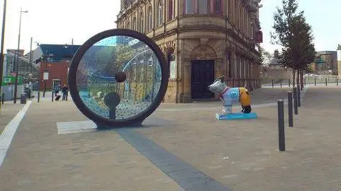 The Propellers of the City artwork in Sunderland's Keel Square. It is a blue and yellow glass circle in a grey frame. It can be rotated like the steering wheel of a boat.