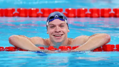 Getty Images  Léon Marchand smiles to the camera from the pool