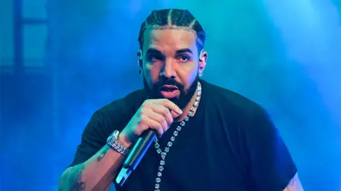 Getty Images Drake, wearing a black t-shirt and holding a black microphone, performs on stage during "Lil Baby & Friends Birthday Celebration Concert" at the State Farm Arena.