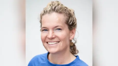 Jim Fanning Charlotte Carson has curly blonde hair tied up and wearing a blue top, she is sitting in front of a white screen.