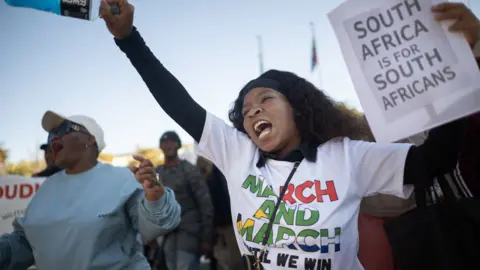 A woman punches the air, while holding a placard reading "South Africa is for South Africans" during an anti-migrant march.
