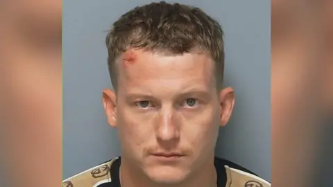 Toby Lucas' mugshot. He is wearing a black and sandy coloured T-shirt.