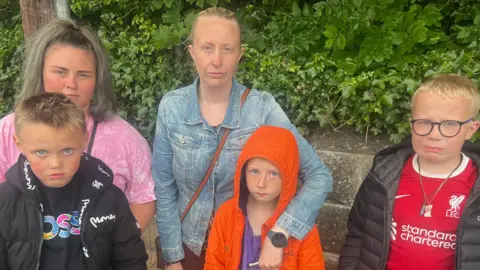 Candice Bunting and Shelley Ritchie along with their children who are aged 9, 8 and 8. They are standing in the rain.