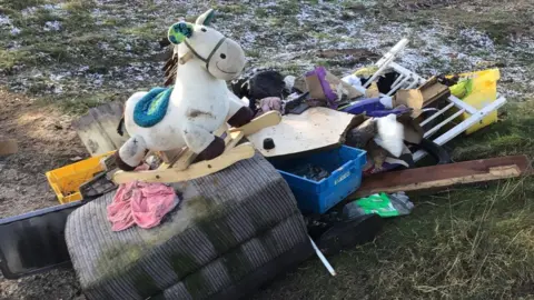 East Riding of Yorkshire Council Items dumped in a heap on snowy grass. Among them are part of a grey sofa, a white rocking horse, a white gate, and several pieces of wood and boxes.