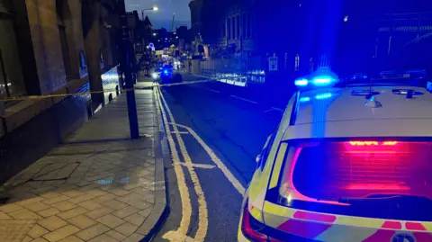 A police tape cordon across Great George Street, with a police car in the foreground. 