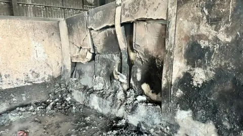 Cambridgeshire County Council The burnt interior of a waste transfer station. It is shows buckled walls blackened walls and grey ash