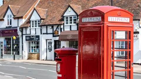 Sara Beaumont Photography A close-up of a red telephone box and a post box on the side of a village high street.